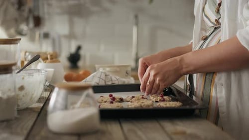 Baking. A middle-aged girl happily places raw cookies on a baking sheet in the oven at her