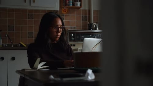 A woman types on her notebook computer as she sits in her home office setup working in the afternoon