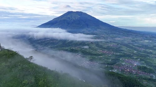 Drone flying over from the top of a hazy mountain shows another mountain.