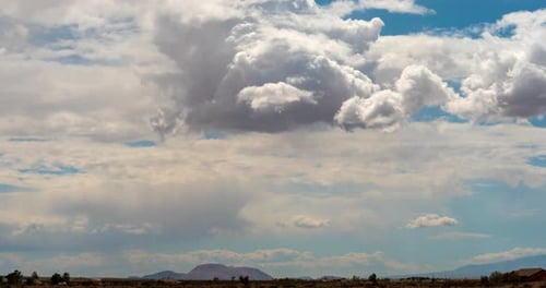 A dynamic cloudscape with abstract shapes forms above the desert landscape - daytime time lapse