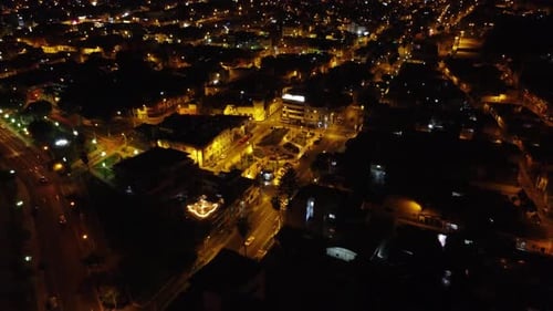 Night time lights shine through a city as drone flies backwards and upwards revealing the entirety o