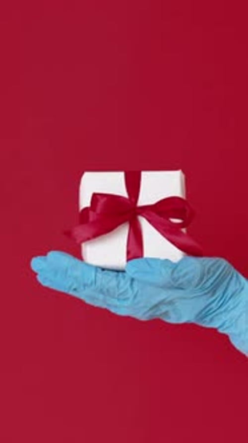 Gift Held by Gloved Hand on Red Background