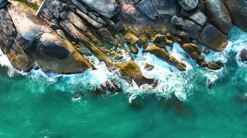 Vue aérienne par drone des vagues mousseuses se brisant sur un rivage rocheux.