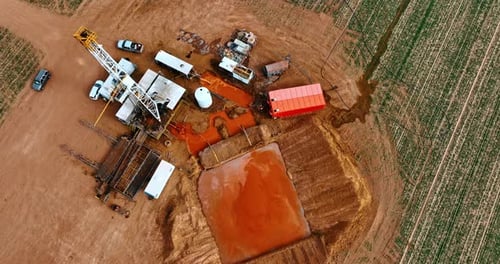 Big square pit filled with orange dirt at the site for drilling oil.