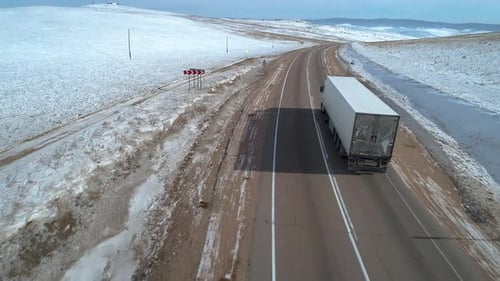 Aerial Shot of a Lorry Truck Driving on an Intercity Road Among the Fields Covered with Snow Winter