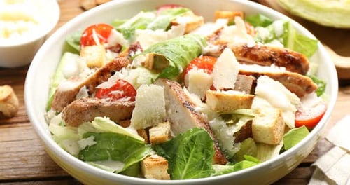 Frau fügt Käse zum Caesar-Salat am Holztisch hinzu, Nahaufnahme