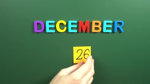 Hand sticking a sticker 26 December calendar day on school board. 26 date of December. Twenty sixth