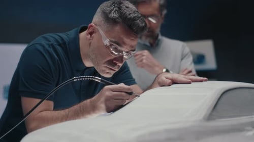 Automotive Engineer Works on Sculpture of a Car While Discussing with Colleague