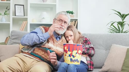 Grandfather and Granddaughter Watch Scary Movie with Popcorn