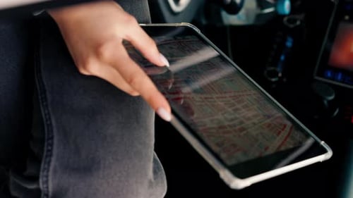 Close-up shot of a girl sitting in a car plotting a route through the forest using map on a tablet