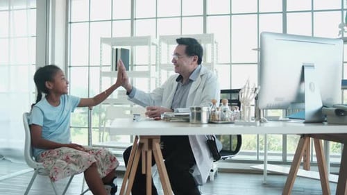 A senior Asian doctor encourages Black patient girl in a pediatric hospital.