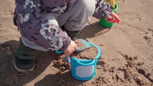Close-up of a child's hands playing with a sand shovel outside.
