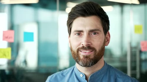 Portrait of a happy bearded businessman in shirt standing at workplace in business office. Confident