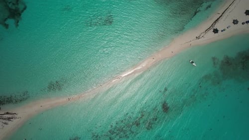 A sandbar in turquoise ocean waters, people and boats visible, bright day, aerial view