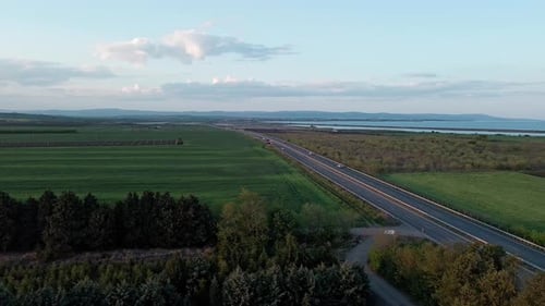 Road with Cars and Trucks on It Passes Through Fields Under a Colored Sky