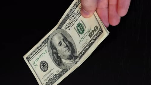 Person putting on table pile of one hundred american dollar banknotes