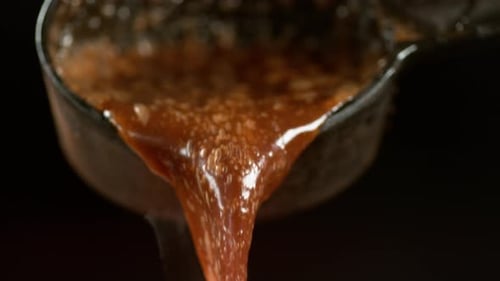 Close-up of glistening brown sauce pouring from ladle