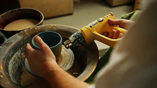 Un potier travaille dans un atelier de poterie en train de sécher un pot en argile crue à l'aide d'un séchoir électrique