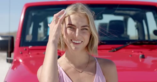 Junge kaukasische Frau lächelt auf einem Roadtrip hell vor einem roten Fahrzeug