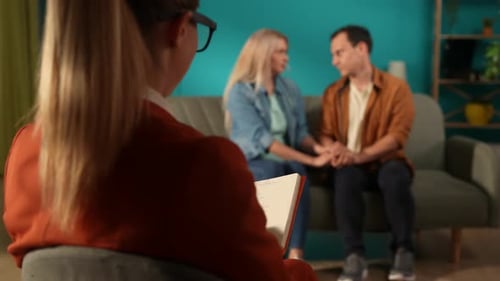 Family Counseling Married Couple Holding Hands Sitting on a Couch in Front of a Female Psychologist