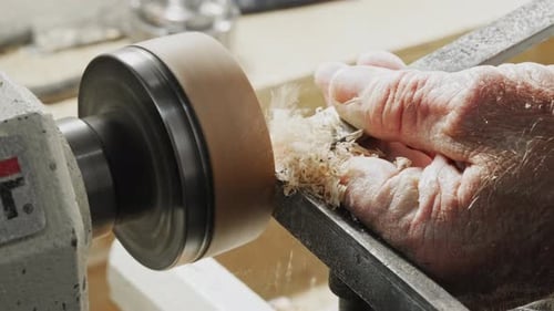 old man using a lathe and chisel to turn and cut a wooden disk