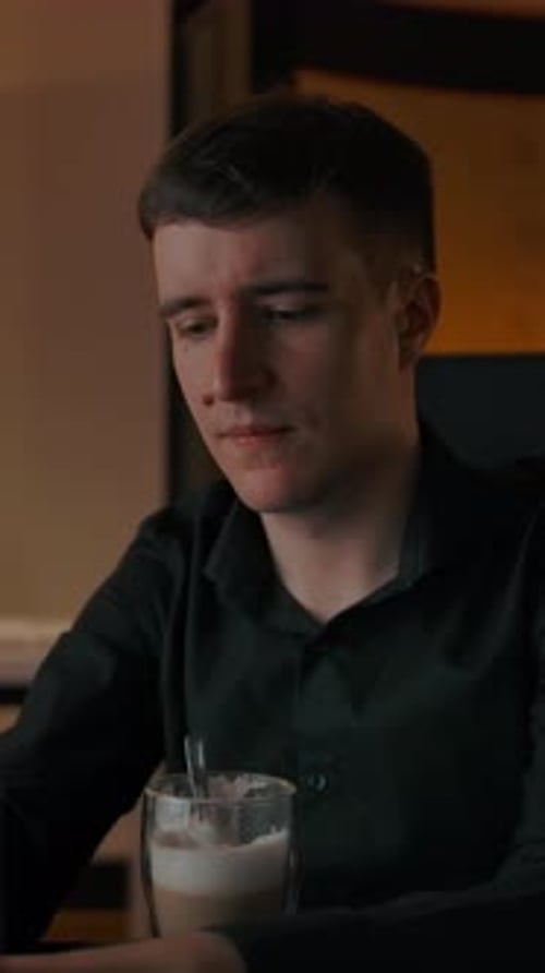 Vertical of Interested Man Drinks Coffee at Home Looking at His Laptop in Living Room