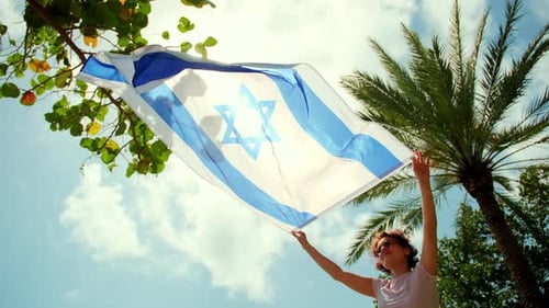 A Woman Holds the Israel Flag Against a Strong Wind with a Background of Clear Blue Sky and Tropical