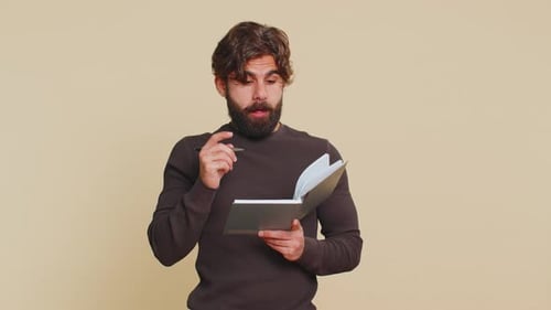 Man Writing in Notebook With Pen Against Plain Backdrop