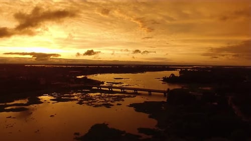 Drone descending over the river at sunset in golden hour with bridge in background