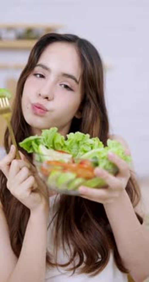 Teenage asian girl smiling brightly and presenting glass bowl of green salad with fresh...
