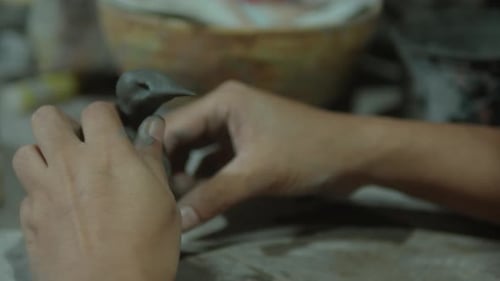 Hands shaping clay in a close-up, creating detailed pottery