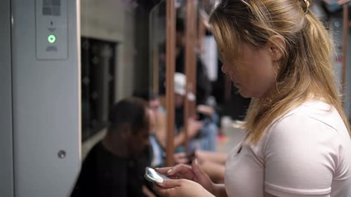 A Young Woman with a Phone in Her Hands in a Full Subway Car