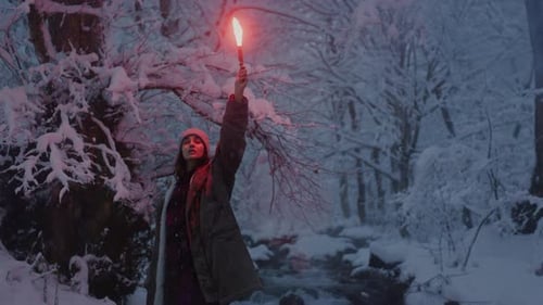 The Girl Holds a Red Burning Signal Light in Her Hand A Woman in a Snowy Winter Forest Trees