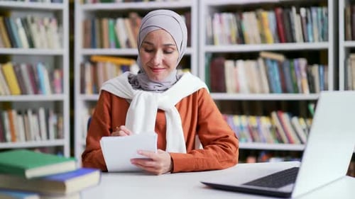 Woman Studies and Takes Notes in a Library