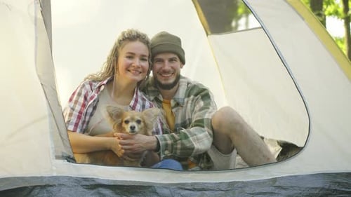 A Couple in Love Enjoys Relaxing in a Tent in the Forest While Their Playful Chihuahua Dog Rests at