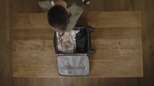 Person Packing Suitcase on Table Overhead