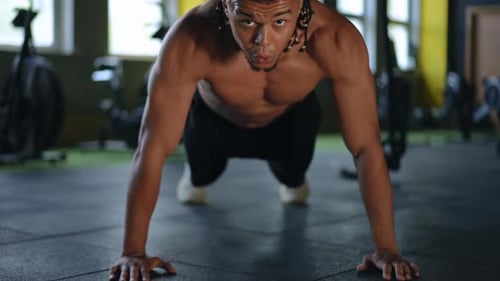 Closeup A Mixed Race Man with Dreadlocks Looks at the Camera and Does Pushups in a Modern Gym