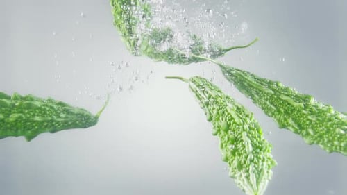 Des melons amers tombant dans de l'eau avec des bulles.