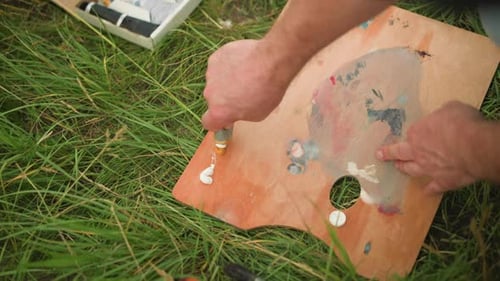Artist's Hand Pouring Paint on Palette in Grassy Field