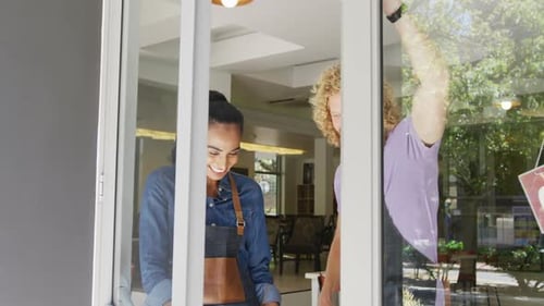 Portrait of happy diverse male and female baristas standing in doorway of their coffee shop