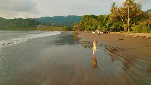 Woman walking along wide sandy beach at sunset in tropical Costa Rica