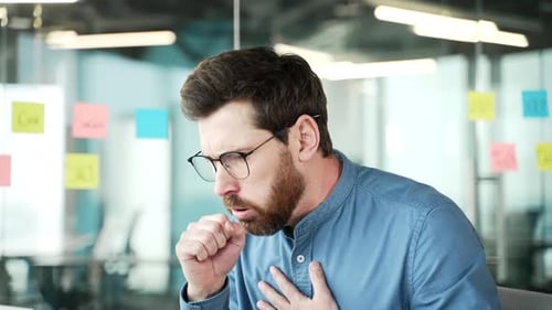 Tired businessman coughing sitting at workplace in business office. Sick with cold or flu employee