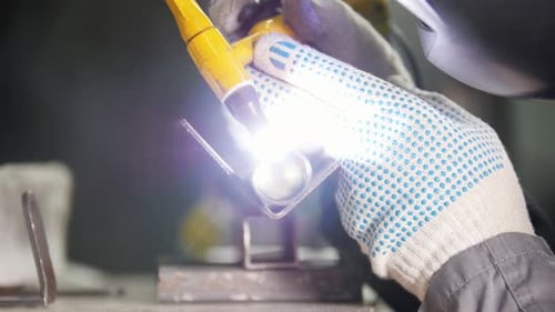 Industriefabrik Ein Arbeiter in Handschuhen schweißt Detailarbeiten