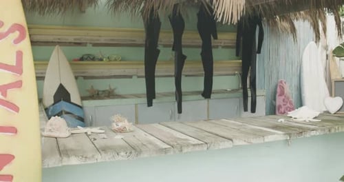 Surfboards and hanging wetsuits in surf rental beach shack, slow motion