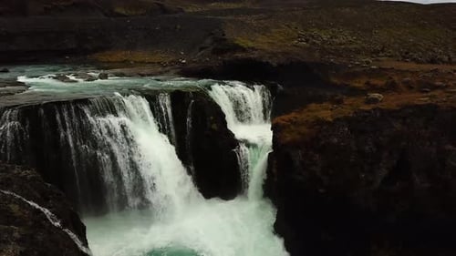 Aerial drone view over water flowing down a large waterfall, in Iceland
