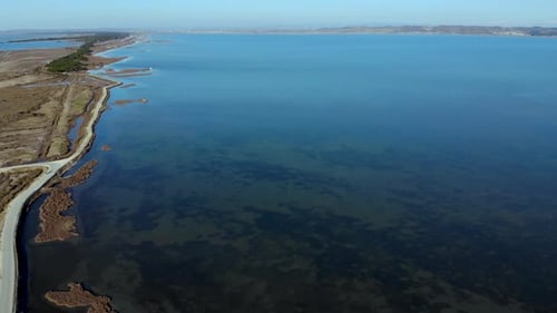 Shallow lagoon with calm clear water bordered by swamp inside beautiful coastline with brown dried g