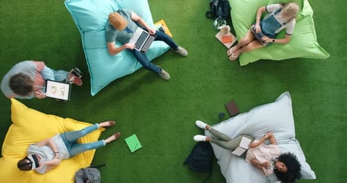 Aerial view of designers using smart technology while relaxing on bean bags in a casual