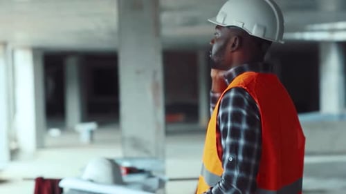Busy Professional AfroAmerican Male in Orange Signal Jacket and Helmet Communicates Via Phone Nodes