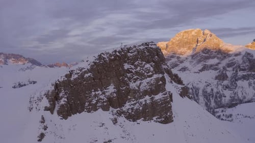 Smooth drone flight around snow-covered summits of mountains lighting in sunlight at sunset - Dolomi