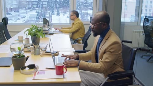 Man in Wheelchair Works on Laptop in Office